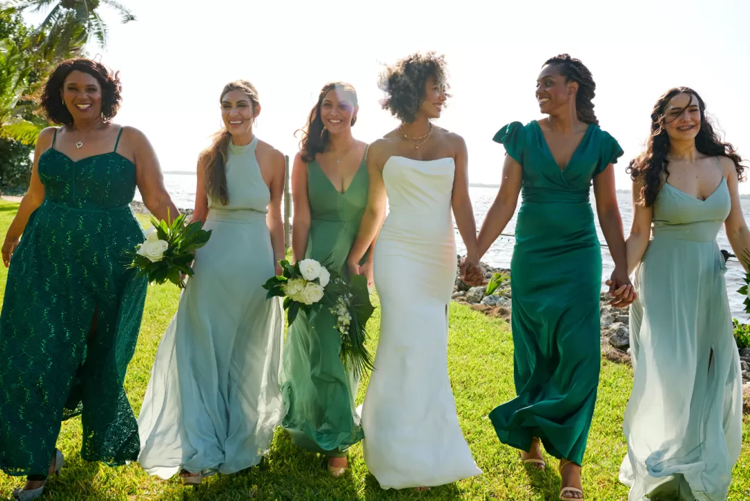 a group of bridesmaids hold hands and walk alongside the river