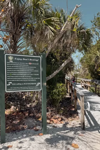 Dark green park sign beside a wooden boardwalk.